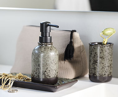 A sink area is organized with a toiletry bag, a toothbrush holder, a soap dispenser, and a tray adorned with jewelry.