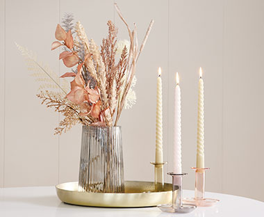 Colourful bouquet of flowers, candlesticks, brass decorative tray and assorted candles