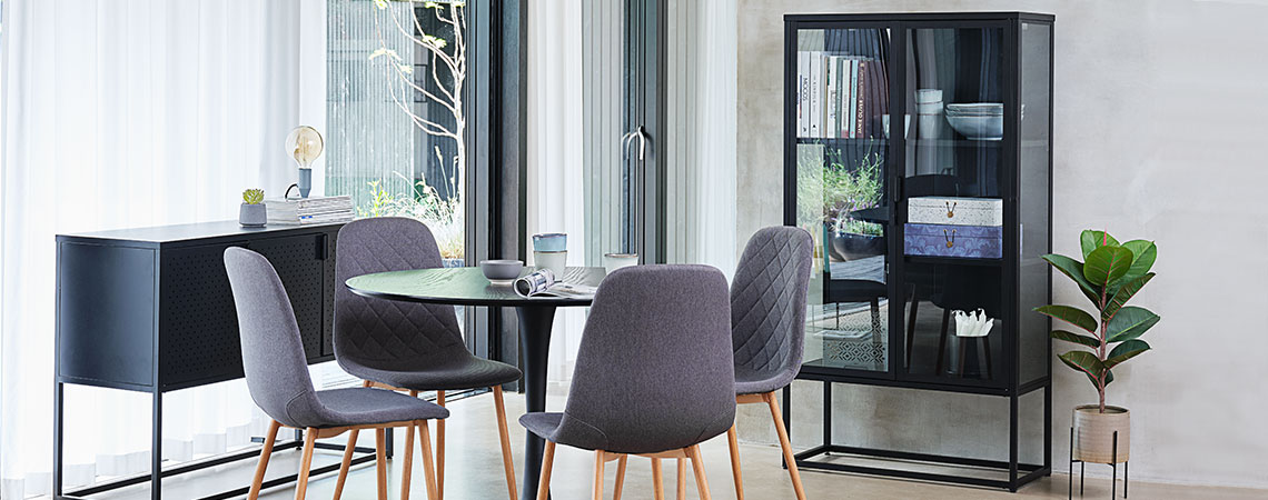 Glass cabinet in a dining room with a round dining table and four grey dining chairs