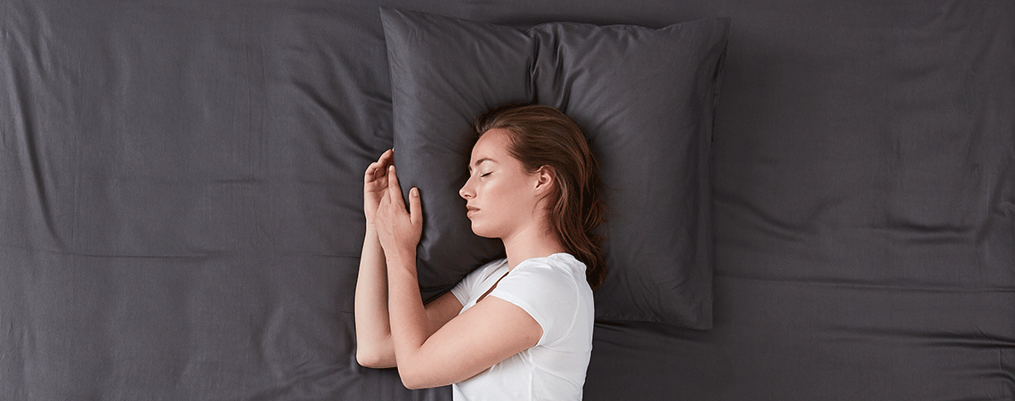 Woman sleeping in bed with dark grey bed linen
