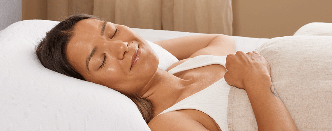 Woman sleeping on her back in bed with pillow and duvet