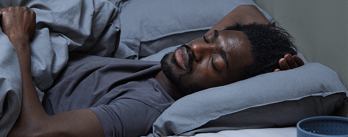 Man sleeping on his back in bed with duvet and grey bedding