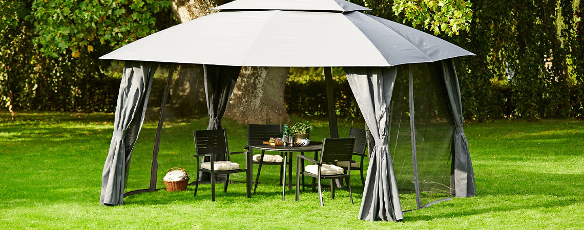 Grey gazebo with dining table and chairs on lawn in garden