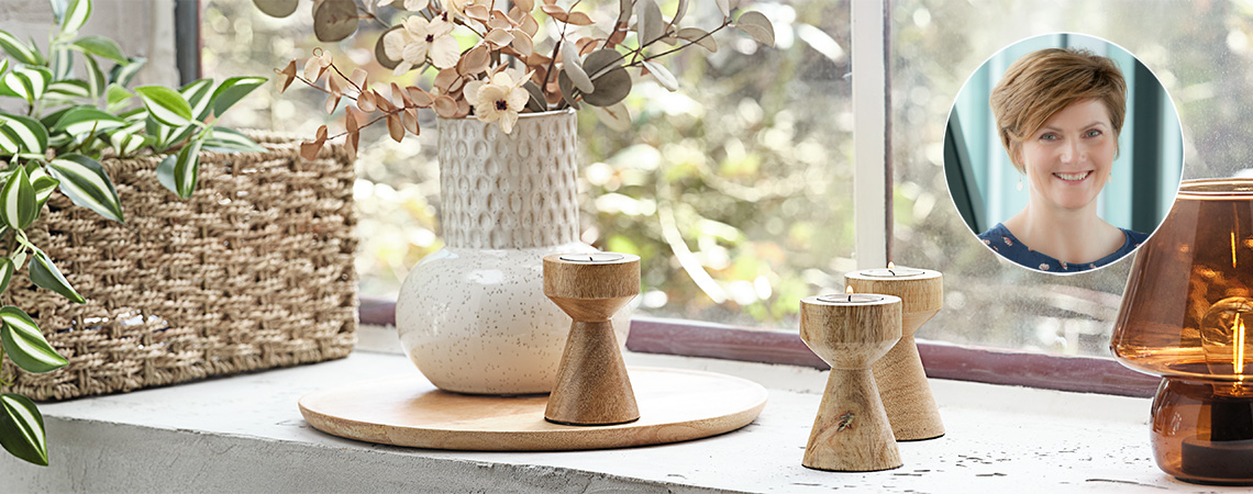 Window sill with lamp, wooden tealight holders, white embossed vase and basket with plant