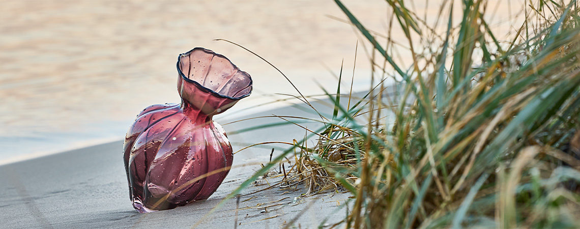 Decorative glass vase in aubergine-coloured glass on beach 