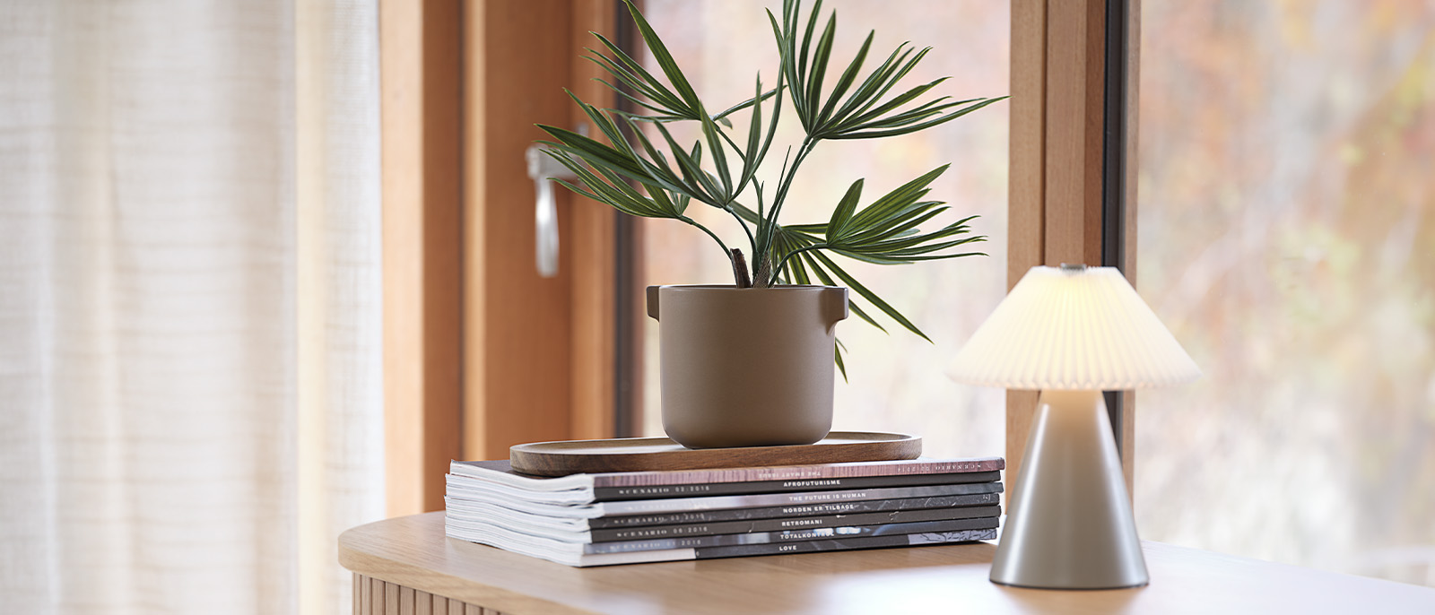 Artificial plant in plant pot on desk with books and table lamp