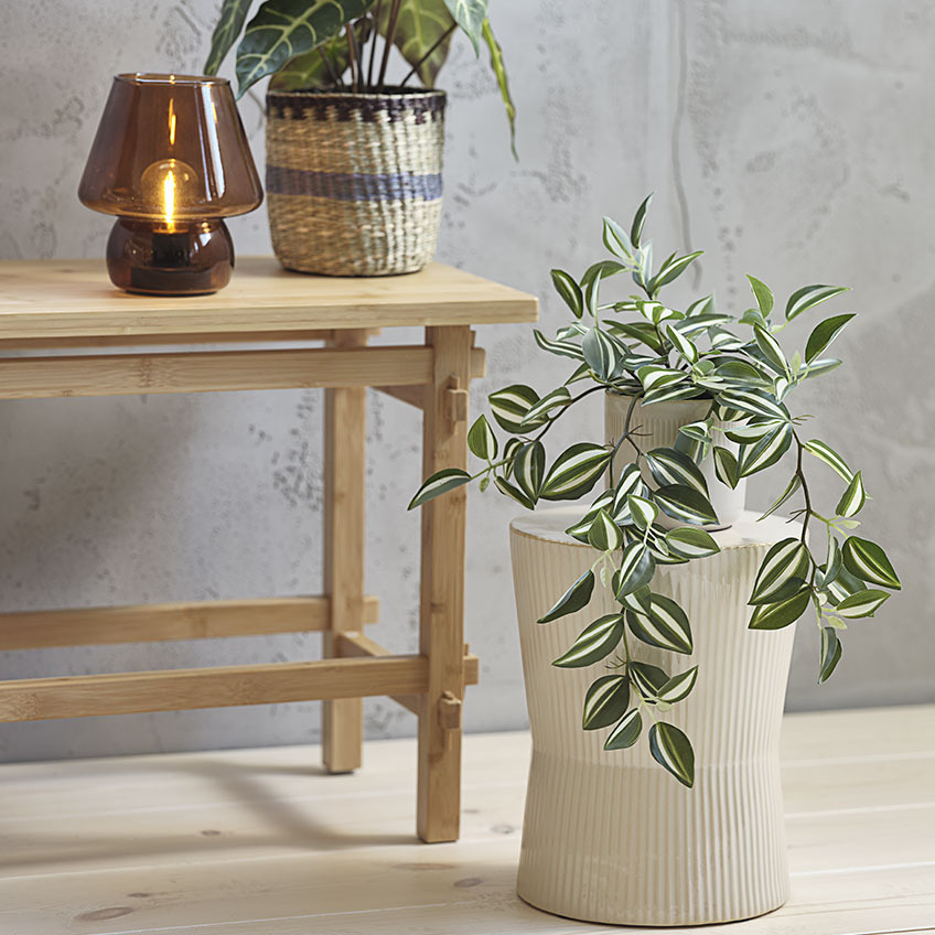 Artificial plant in plant pot on top of white ribbed pedestal 