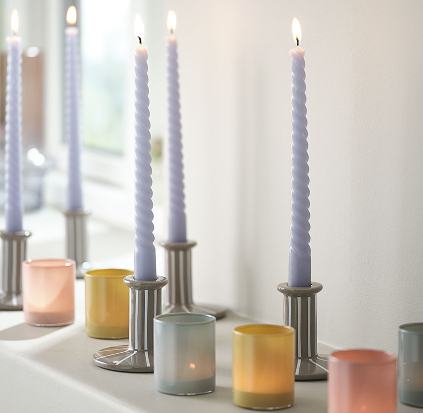 Bright blue twisted candle in candle holder with white stripes, and tealight holders in blue, yellow, and red  