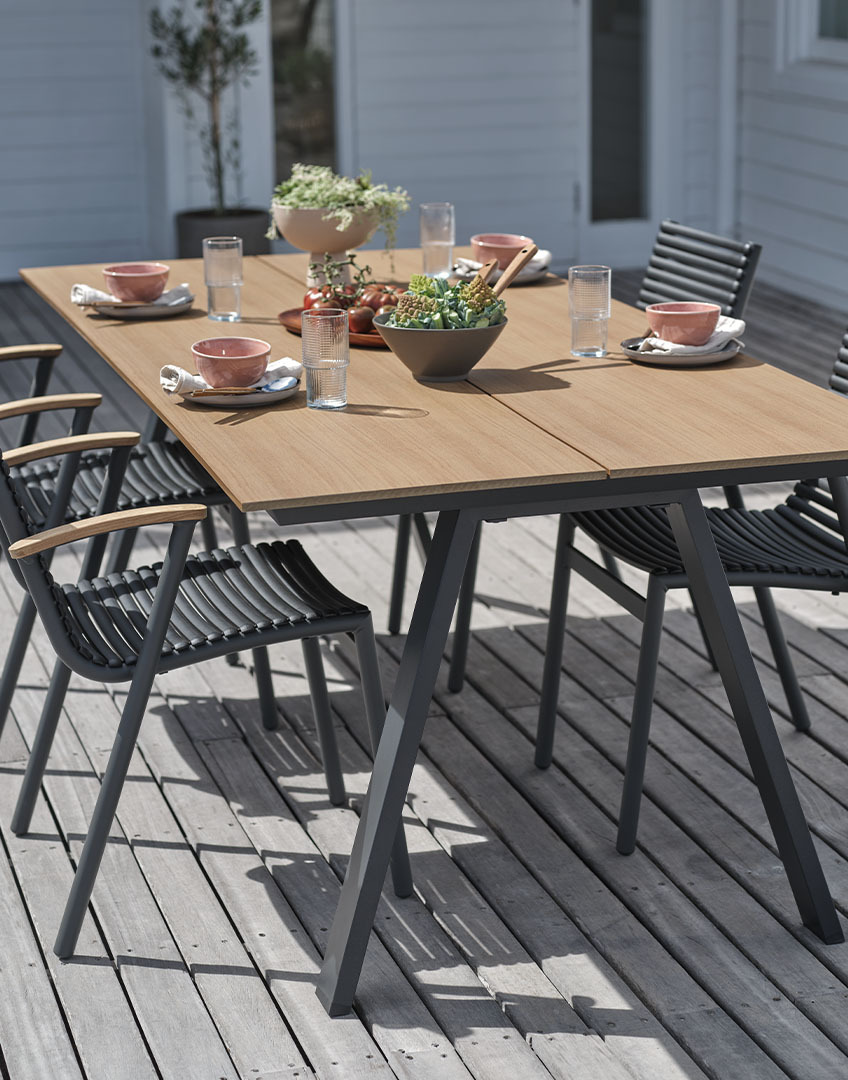 Outdoor table with artificial wood table top and stacking plastic chairs with recycled teak armrests 
