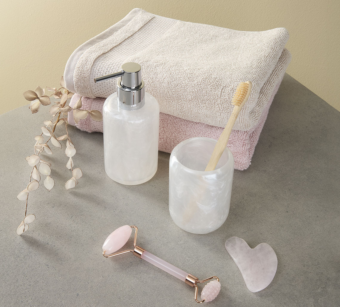 Sand coloured and pink towel next to toothbrush holder, soap dispenser and face roller 