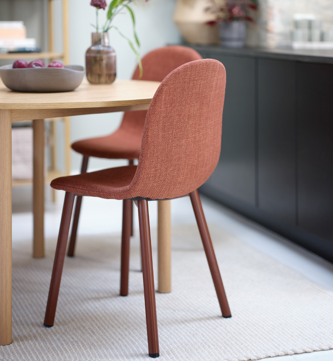 Oak dining table with two terracotta dining chairs on a rug