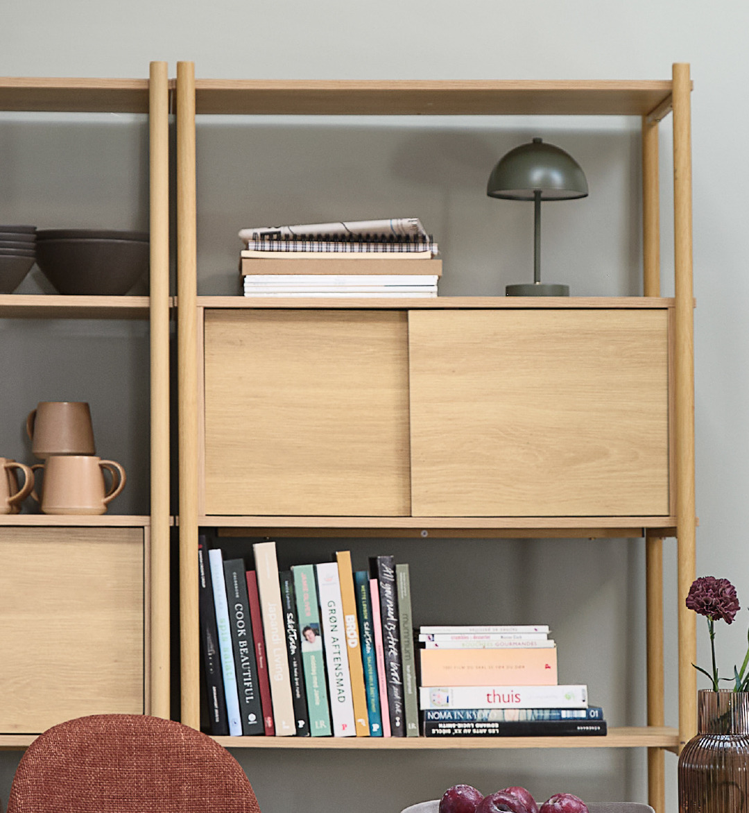 Olive green lamp on oak shelving unit with books and decorations