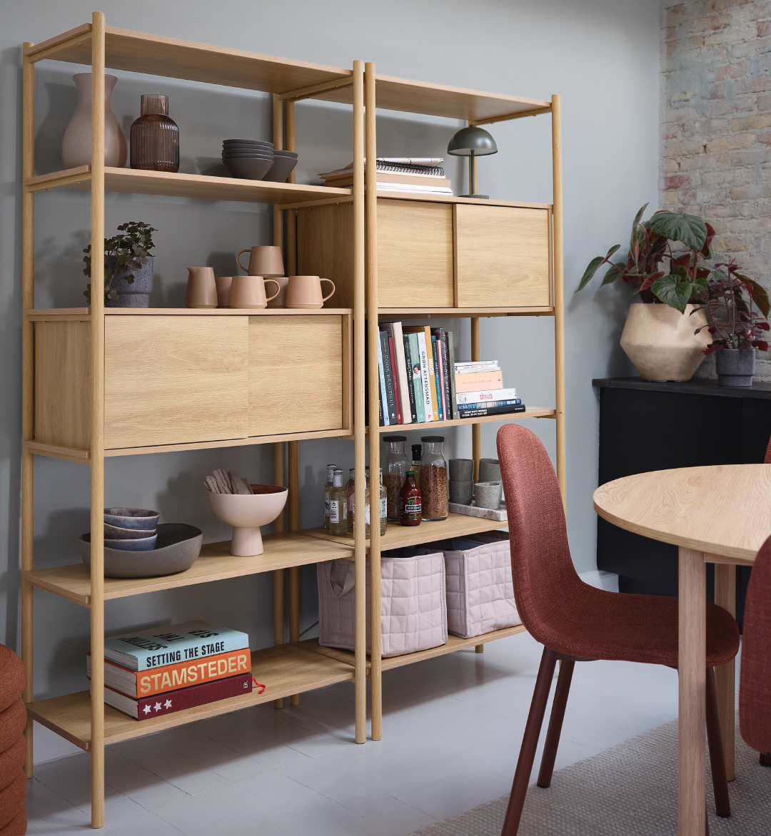 Oak shelving unit with several decorative items next to a dining table with terracotta dining chairs