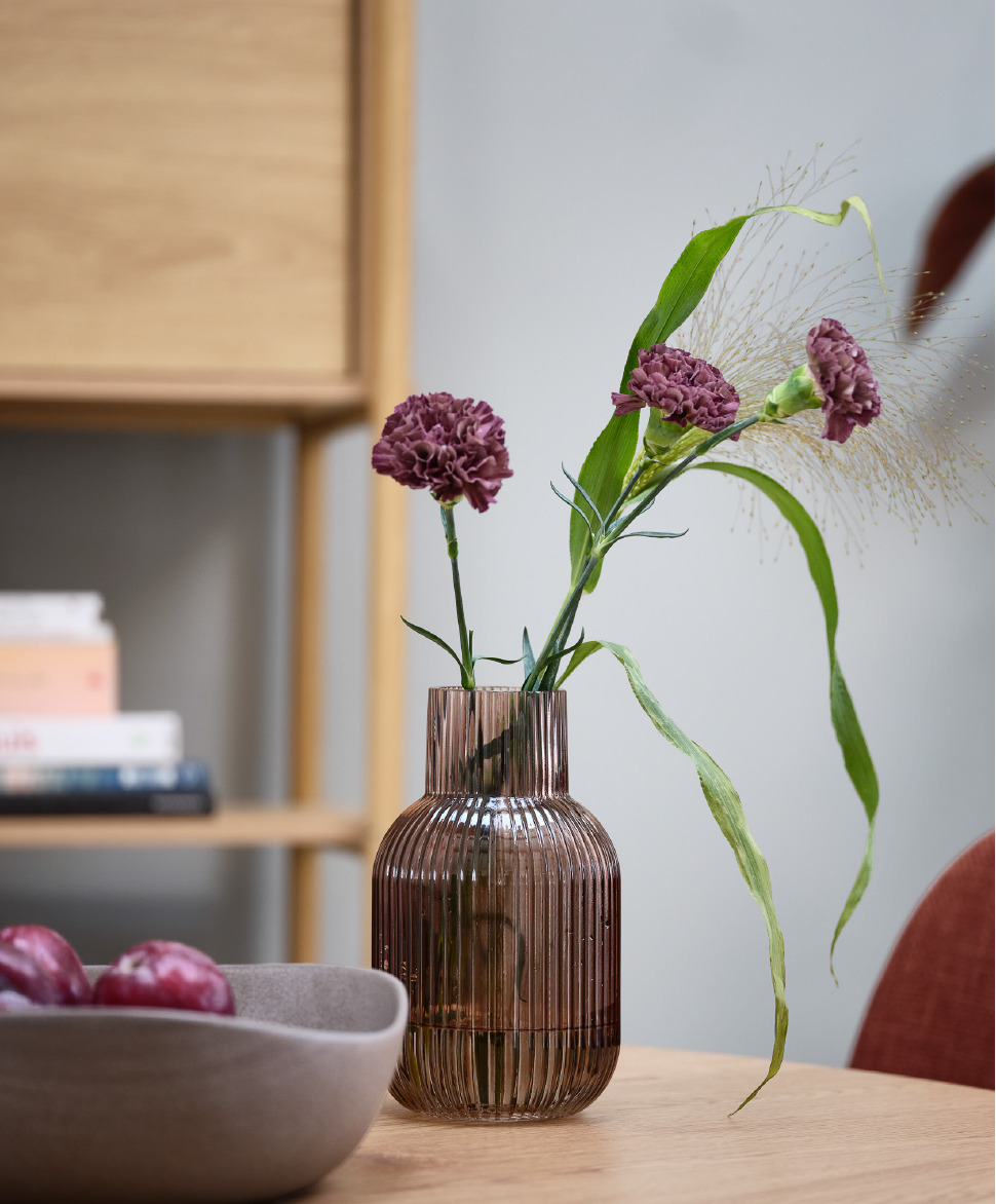 Brown glass vase on dining table with purple flowers