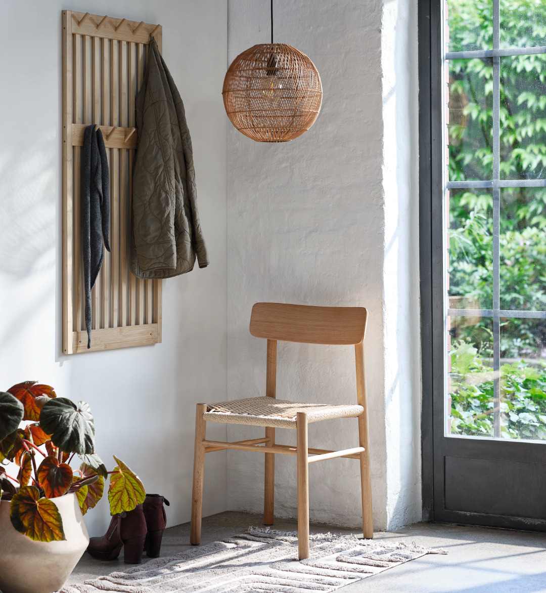 Bamboo coat rack with coat hanging on it next to a weave oak dining chair under a rattan light pendant