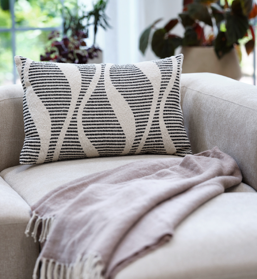 A beige and black decorative cushion on top of a sand coloured sofa