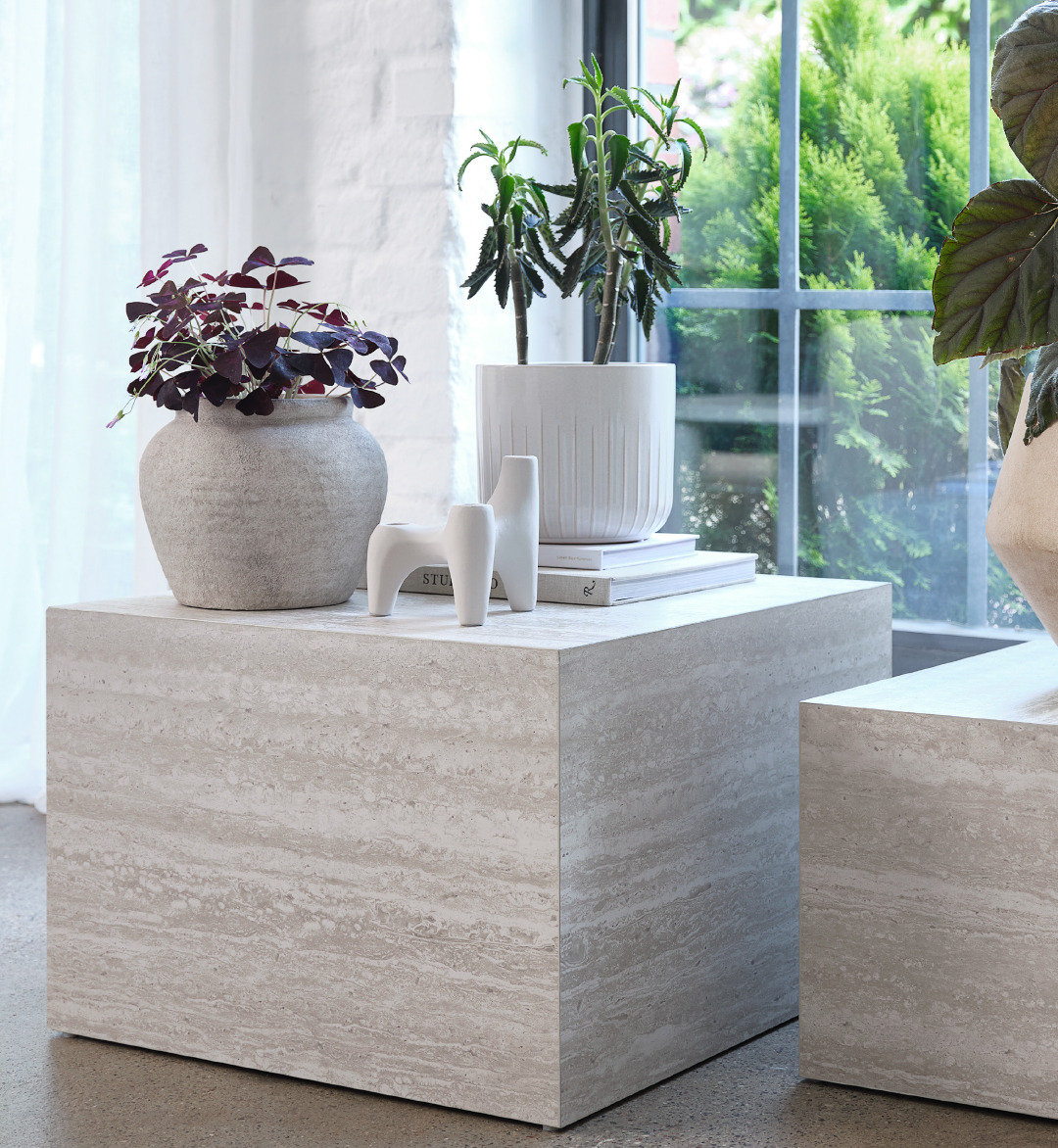 Two plant pots on top of a marble coloured square coffee table and a candle holder