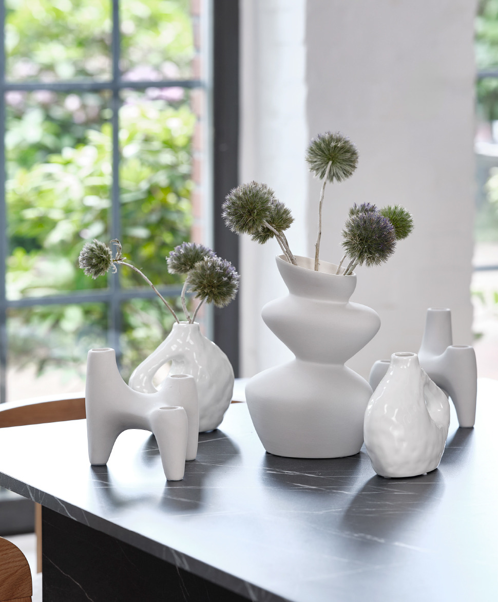 Two white organic shaped candle holders and the vases on top of a black marble dining table