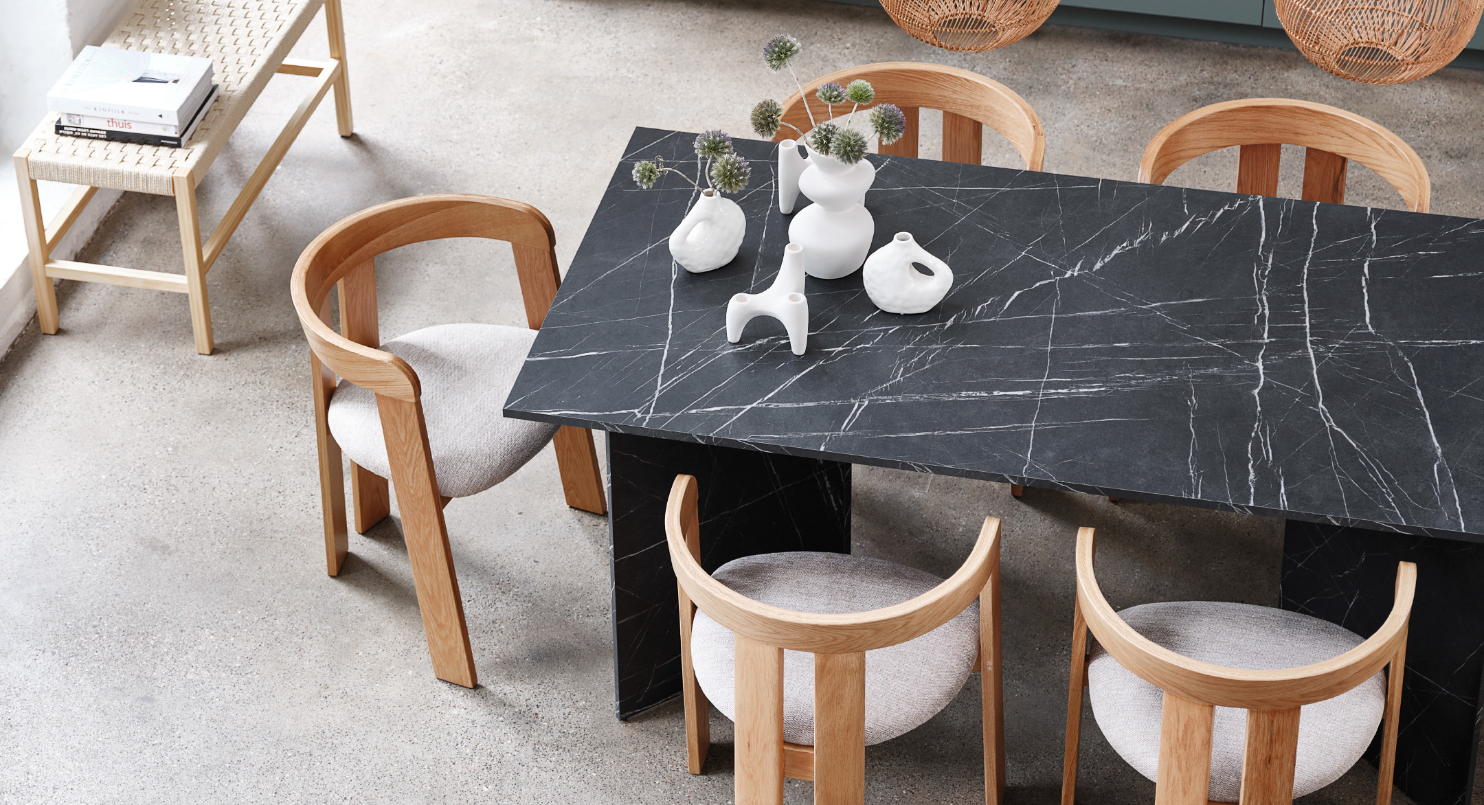 Natural coloured bench next to a black marble dining table and five beige and oak dining chairs