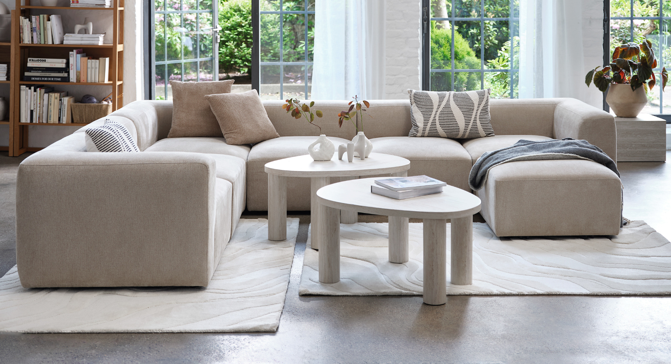 Sand coloured modular sofa set with chaise and pouffe and two marble coloured coffee tables on top of two cream rugs in a living room