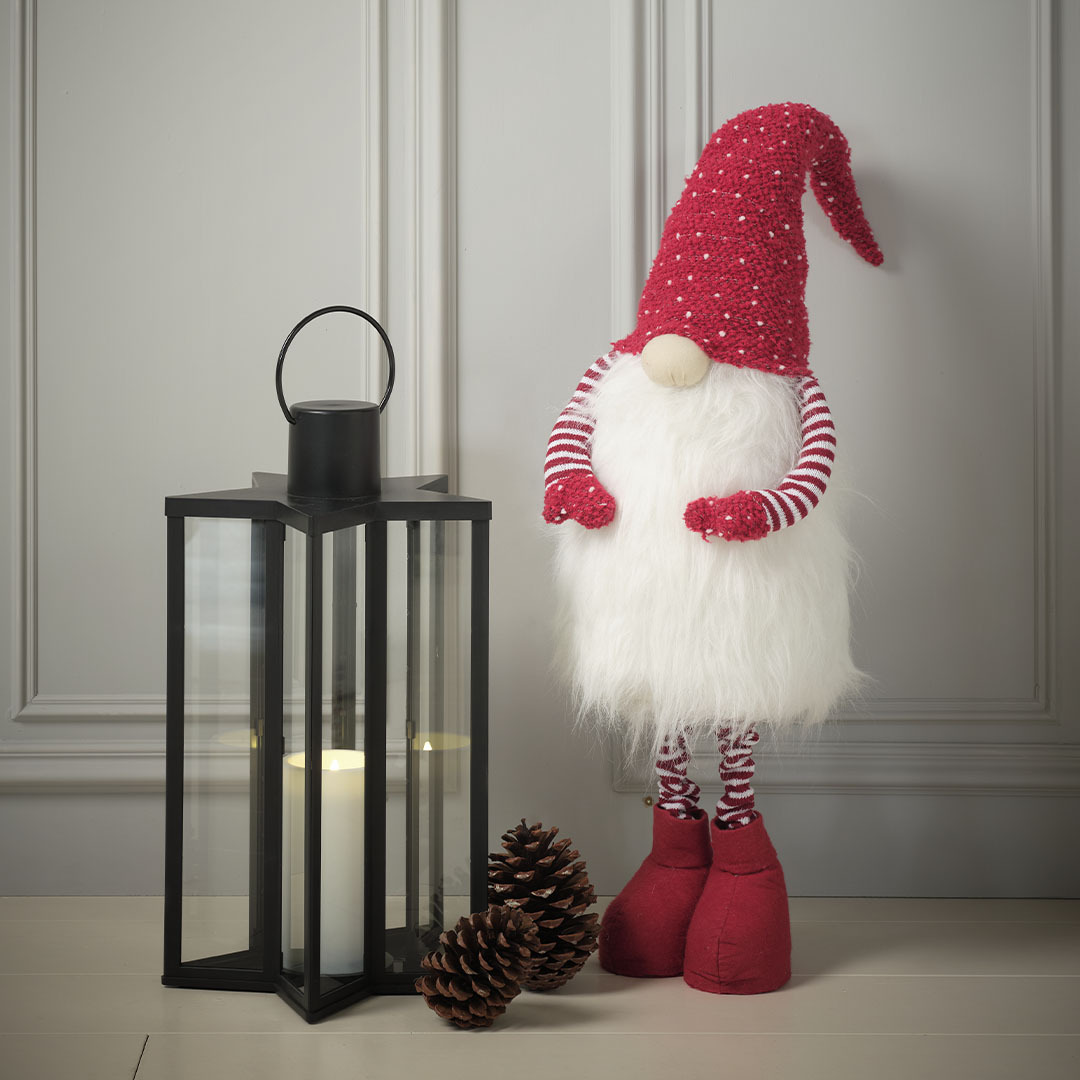 Tall Christmas elf with red hat and big beard next to black, star-shaped lantern 