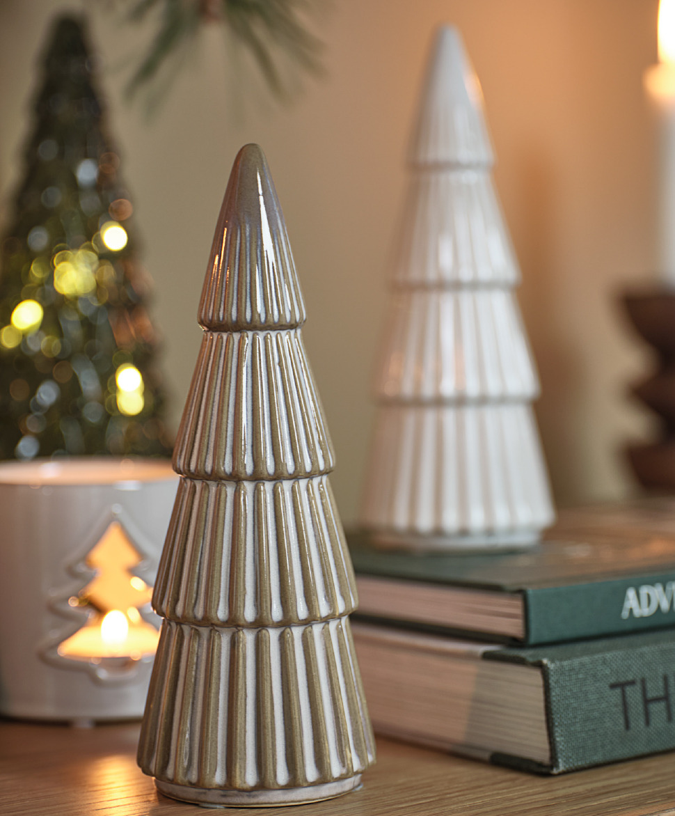 White and brown ceramic Christmas tree decorations on a shelf with a candle