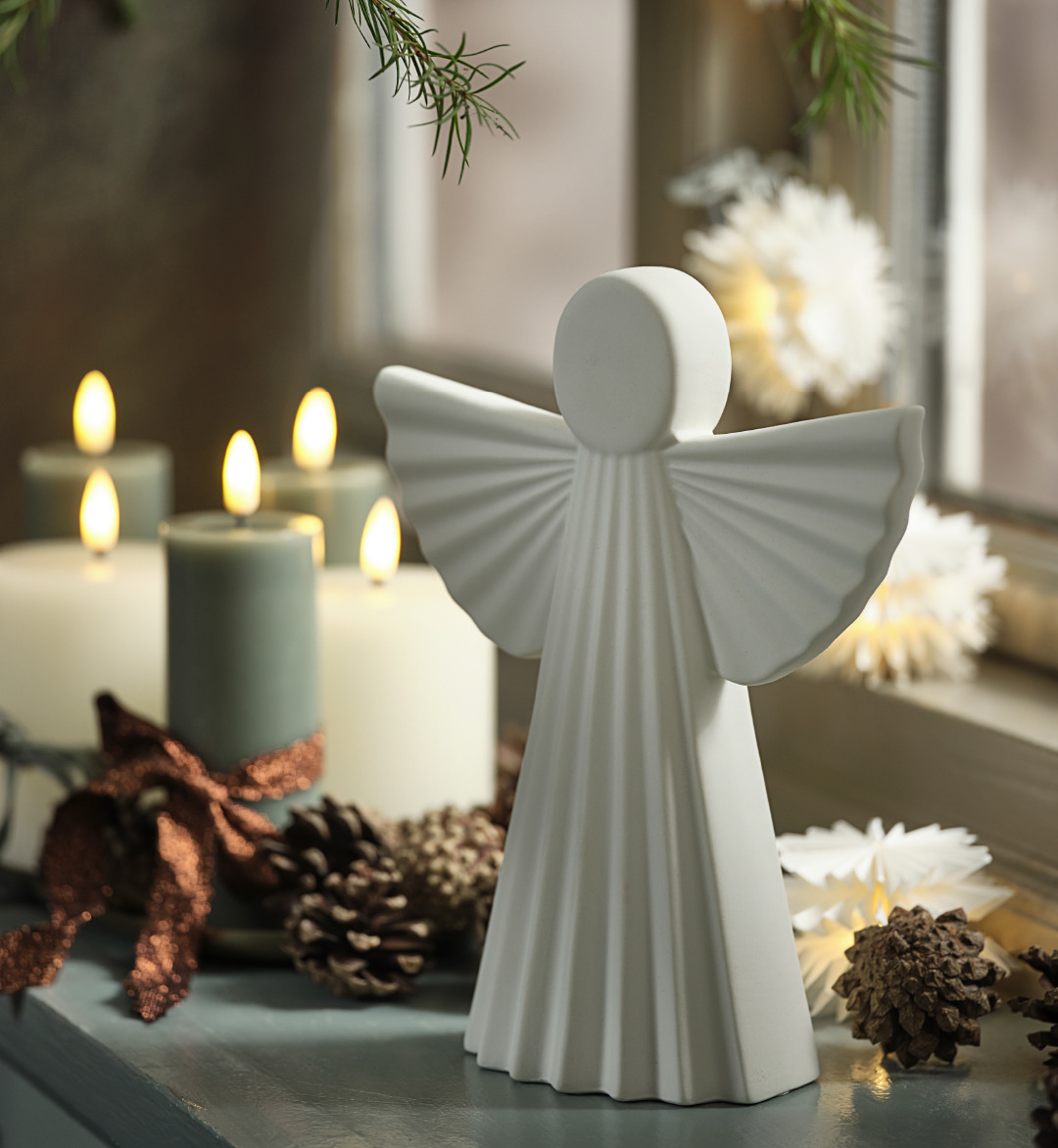 MYS Angel White ceramic decorative angel atop a shelf with lit white and green candles