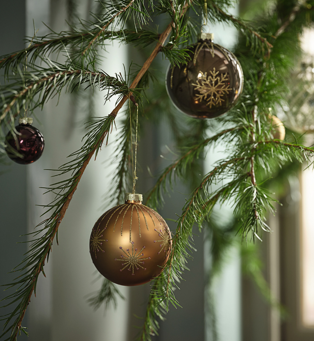 Three gold Christmas baubles hanging off of a Christmas tree.