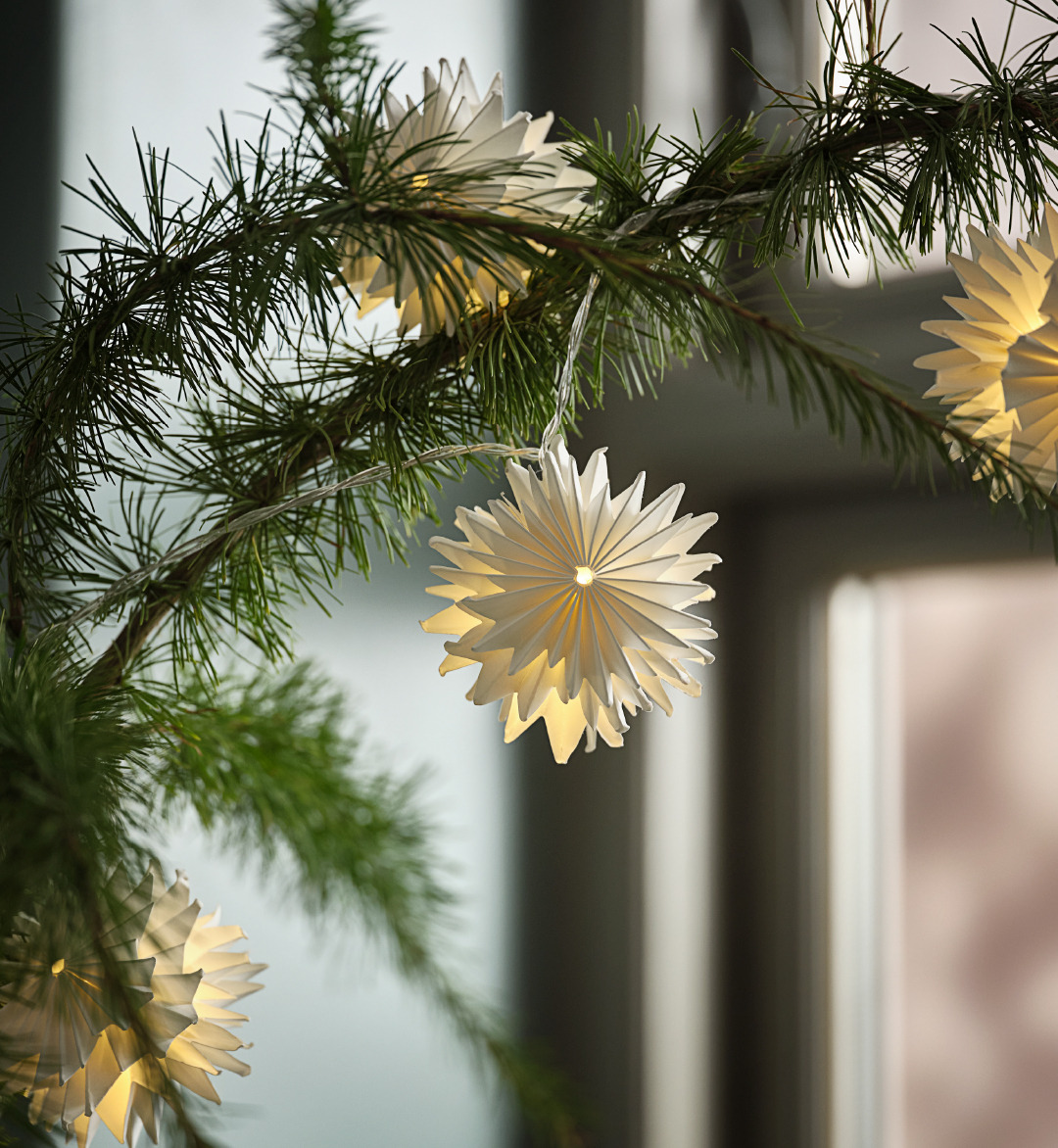 Four white Christmas star decorations hanging off a Christmas tree in front of a window