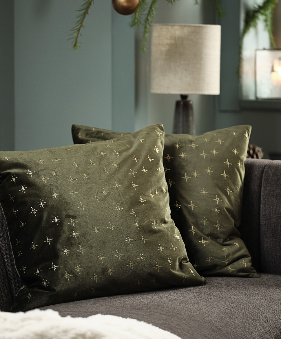 Two green Christmas cushion covers with gold star pattern on a sofa