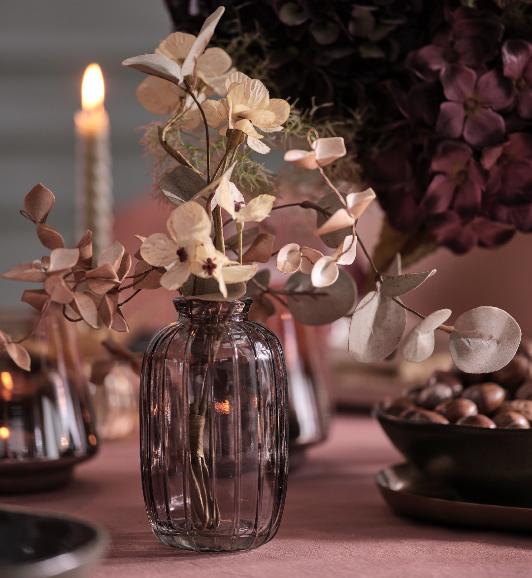 Purple glass vase on top of a dinner table with artificial flowers