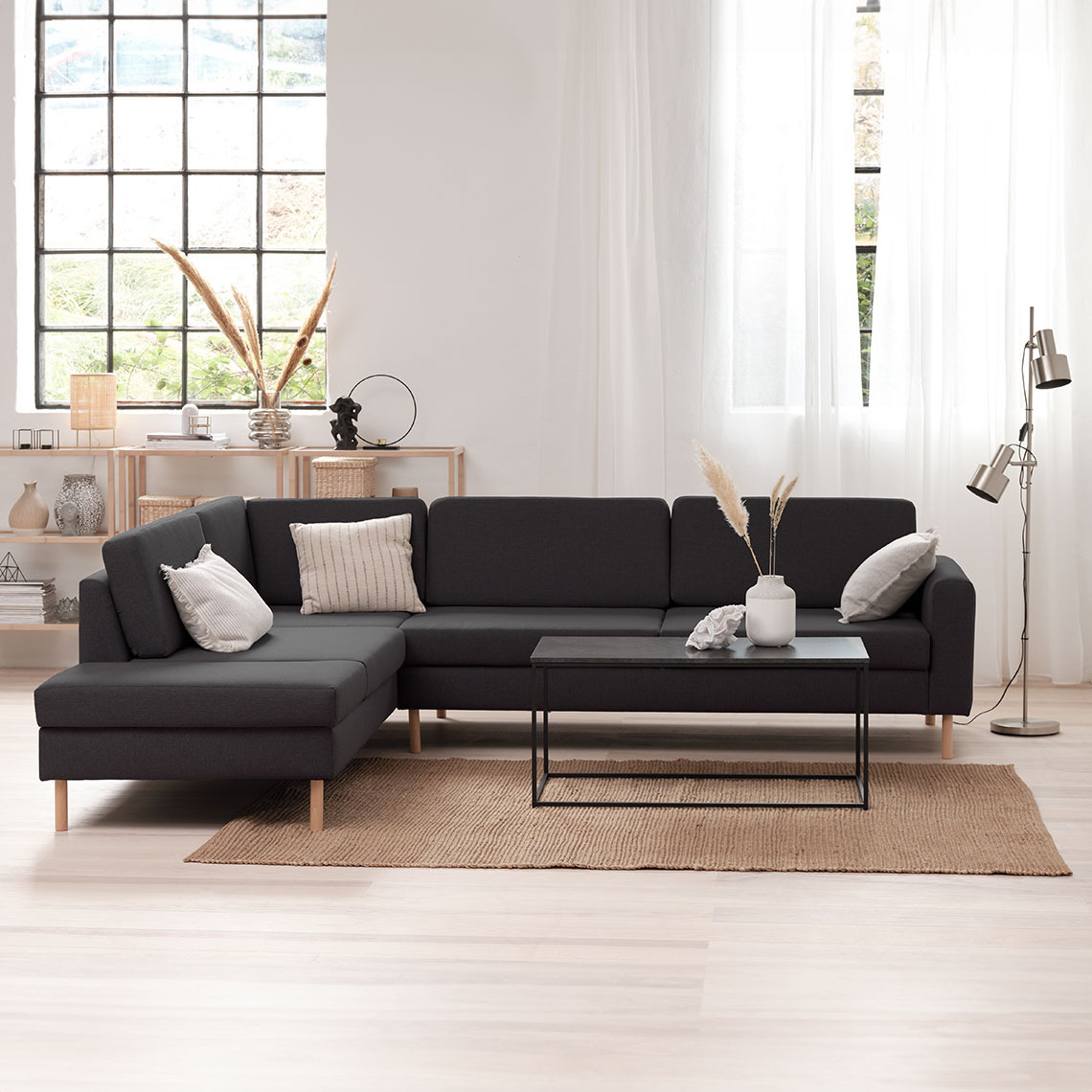 Dark grey corner sofa in a light and airy room with a coffee table and a floor lamp