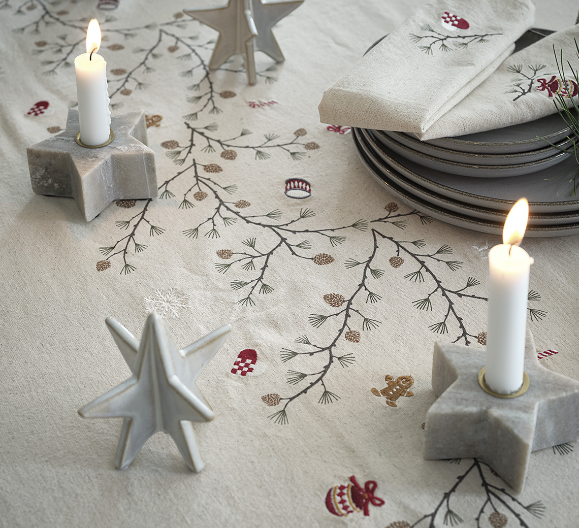 Dining table with Christmas cloth, star shaped candle holders, plates and décor 