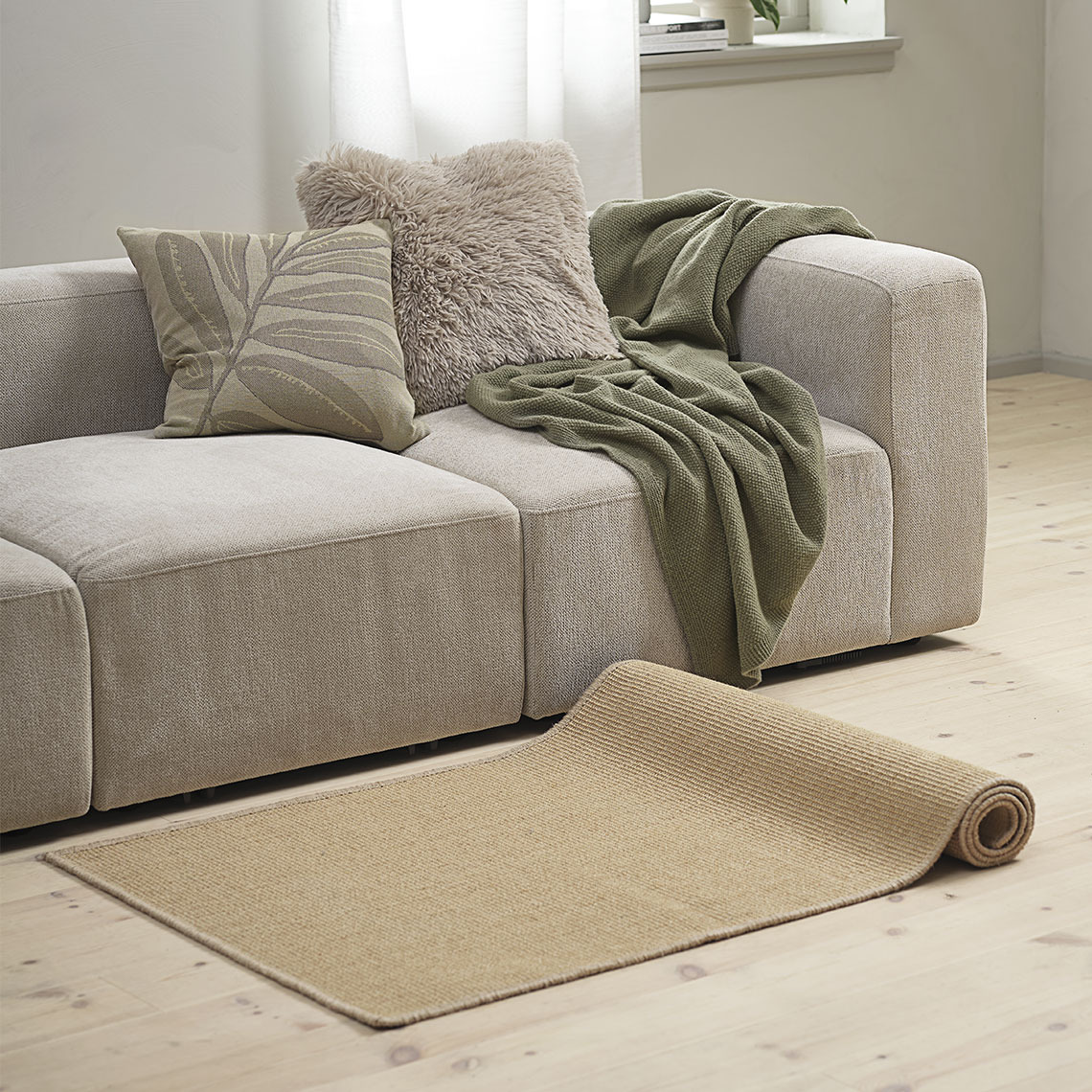 Rectangular beige rug in front of a sofa with soft cushions and a blanket