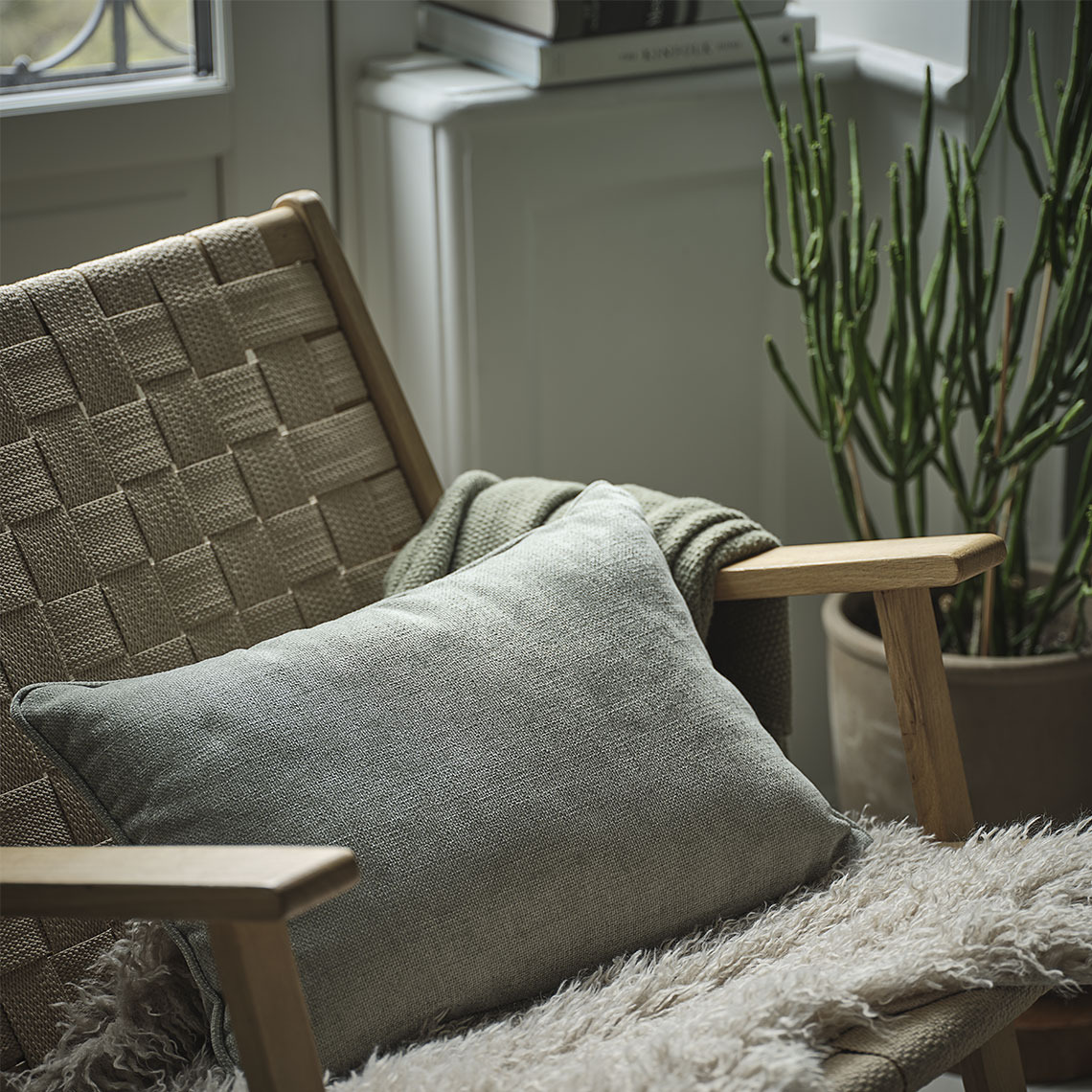 Green cushion in a chair with a green throw and a beige lambskin