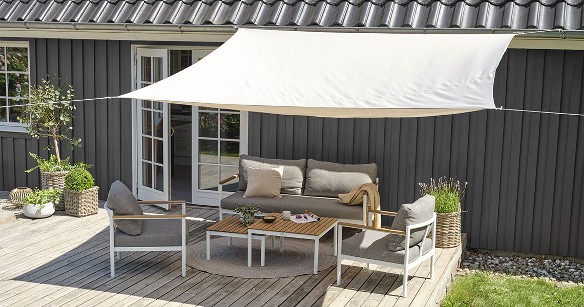 Large shade sail in white above patio with garden table and garden chairs