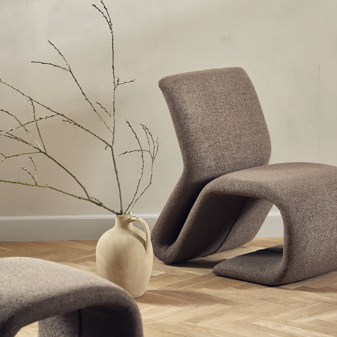 Vase with wood branch on floor next to a modern lounge chair