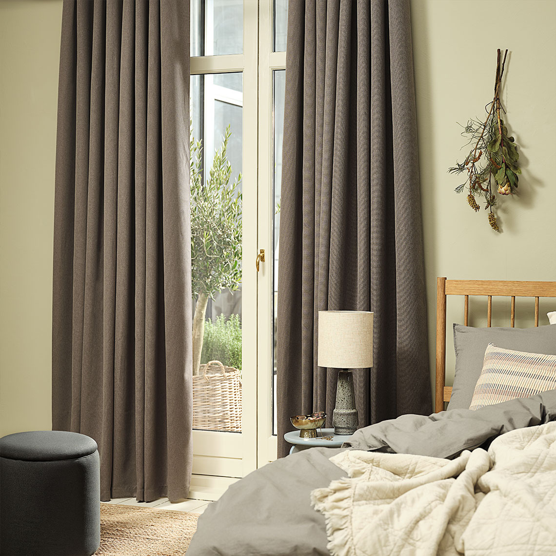 KVINGLA dimming curtain in warm grey  Warm grey dimming curtains hung by a large window in a bedroom