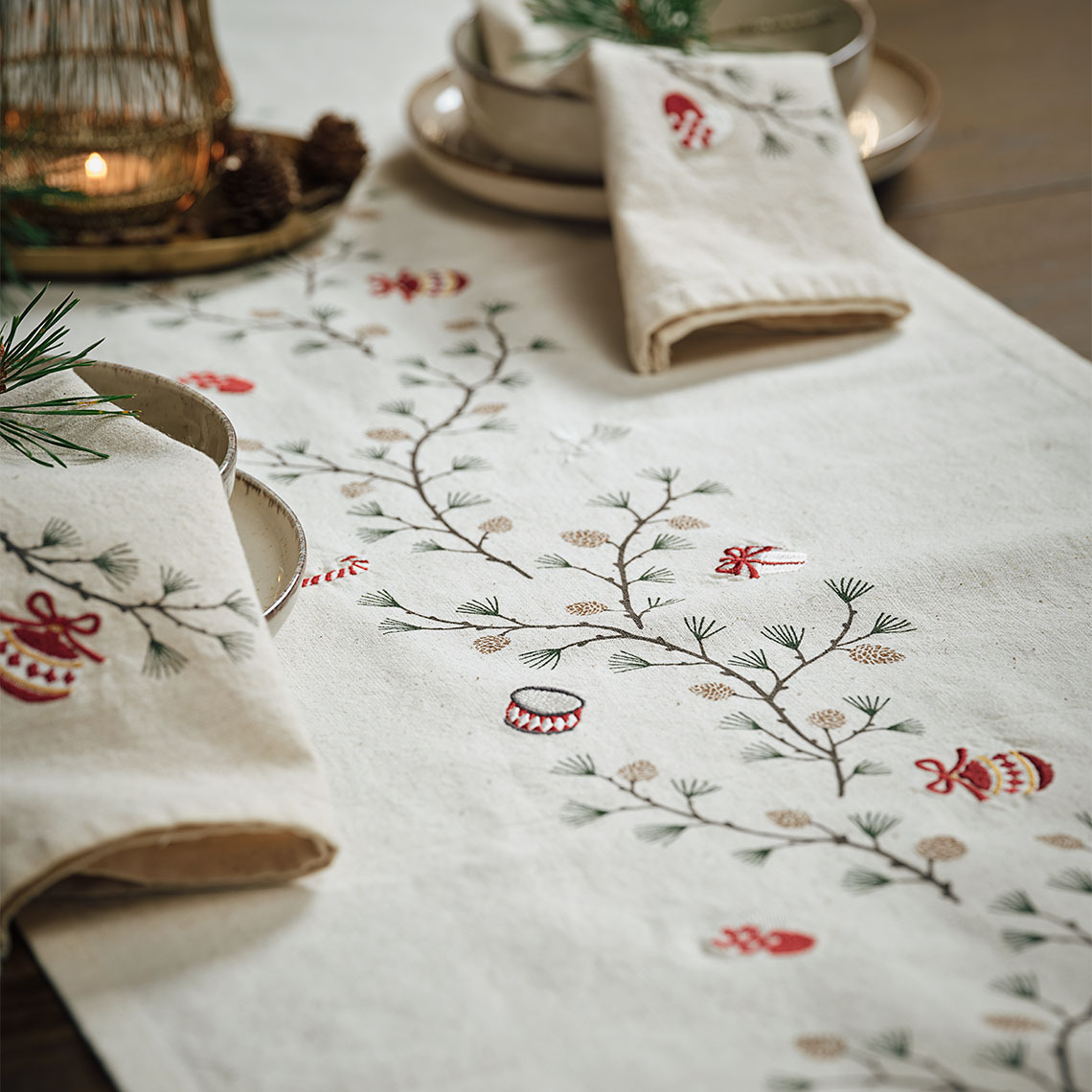 Dining table covered by a Christmas table runner with festive motifs and matching Christmas cloth napkins