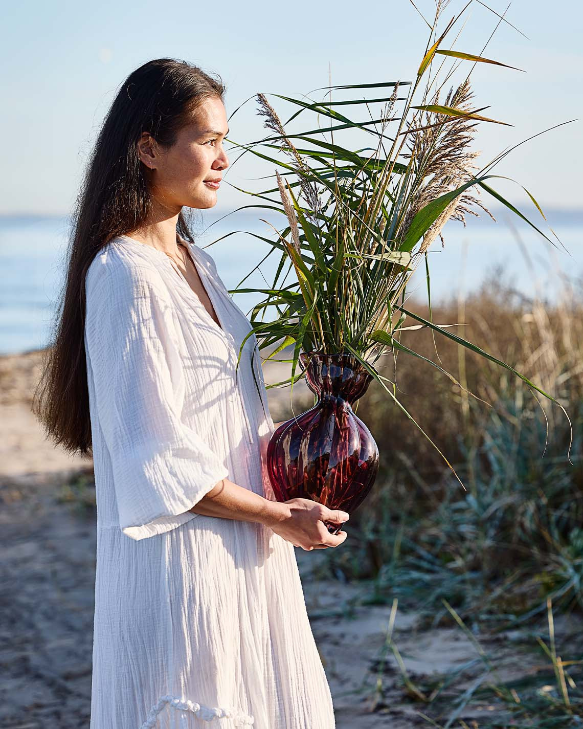 Woman holding glass vase with organic shape on beach 