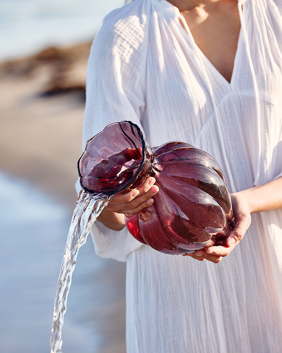 Glass vase in eggplant colour being held by woman on beach