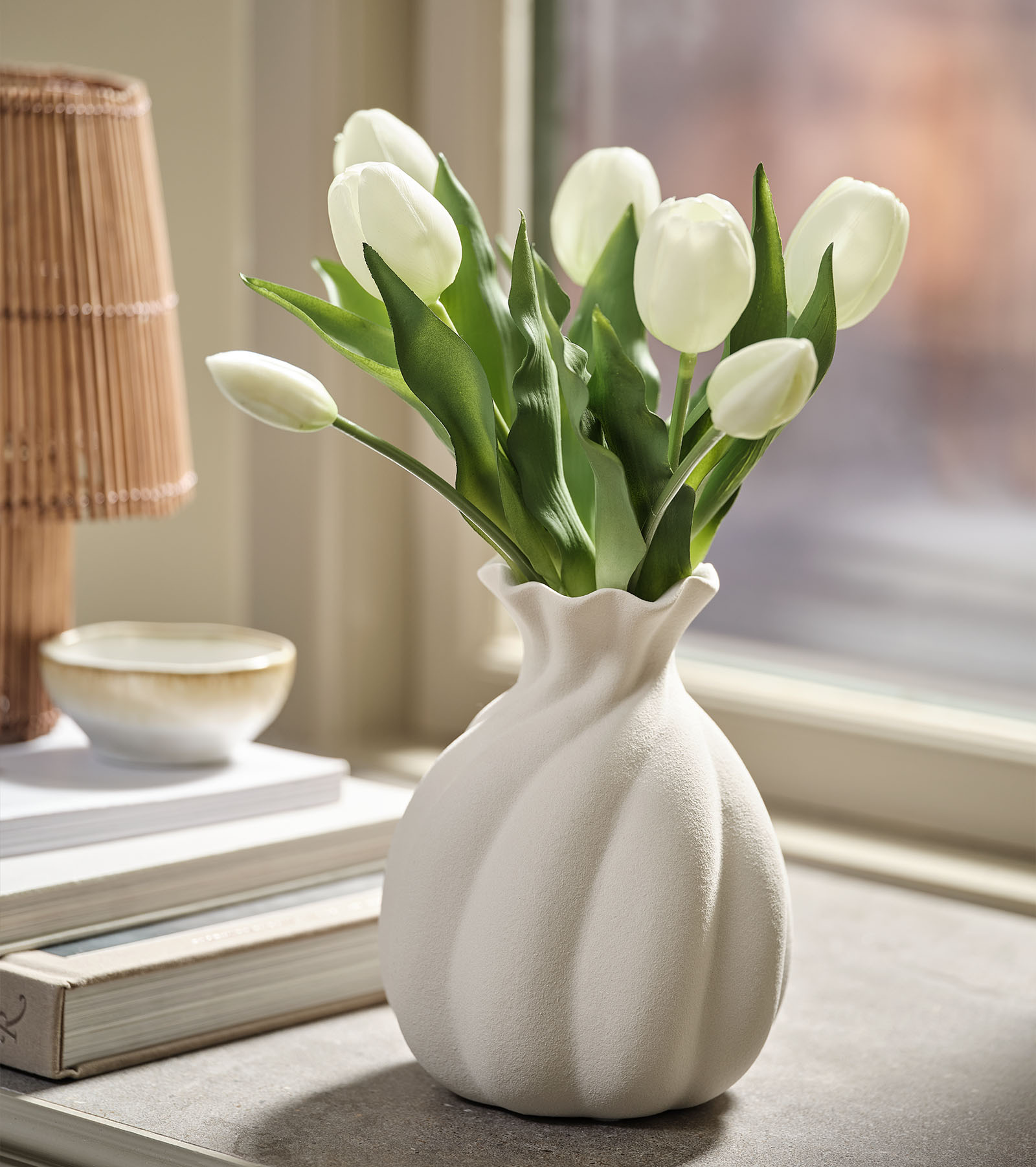 Artificial flower bouquet imitation of white tulips with green leaves in a white vase