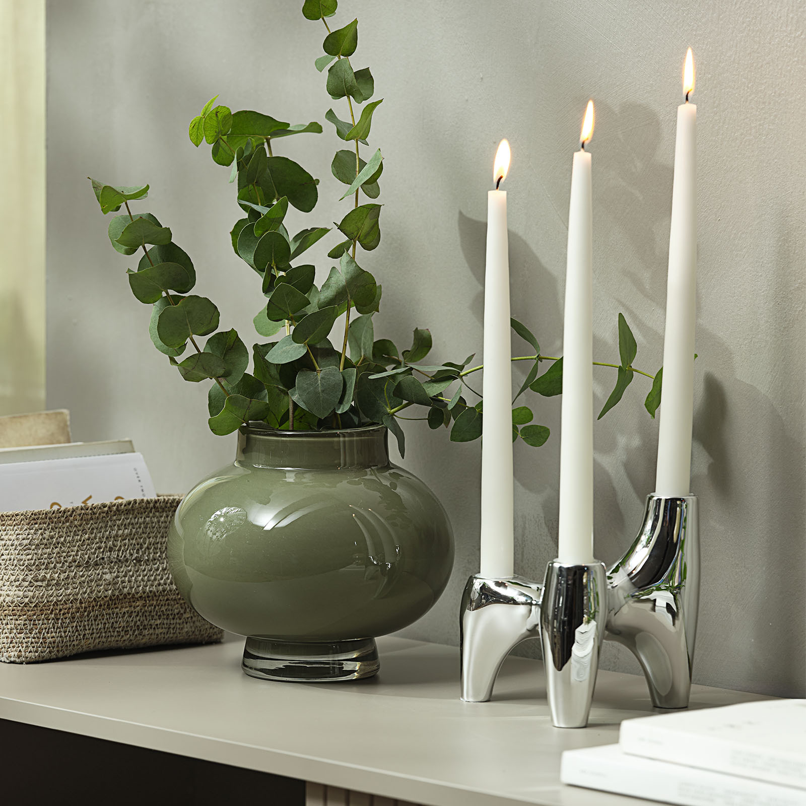 VIGNIR candlestick with chrome-look finish Chrome candlestick holding three candles next to a green glass vase with artificial eucalyptus