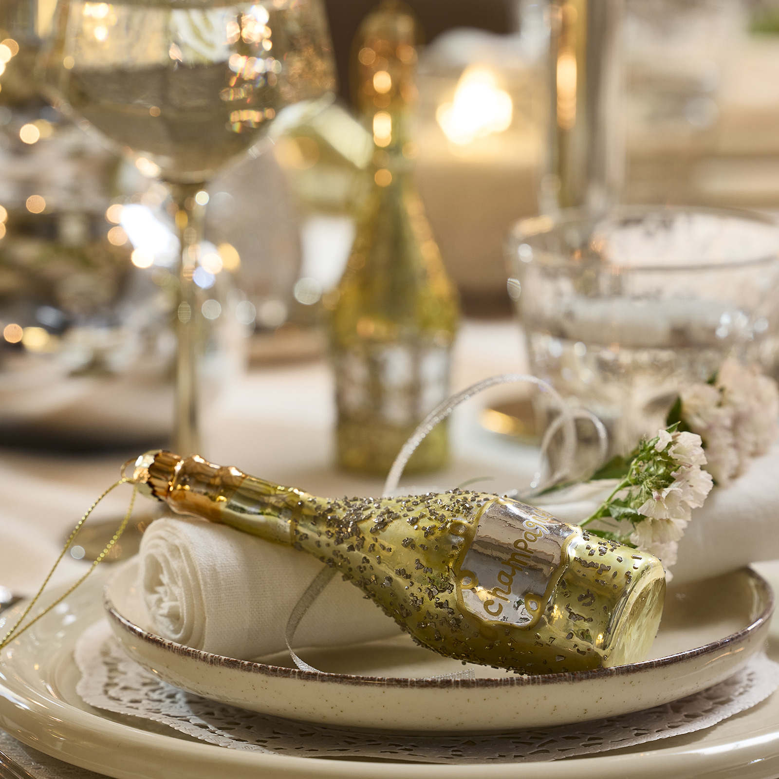 Place setting adorned with champagne bottle shaped Christmas tree decoration 