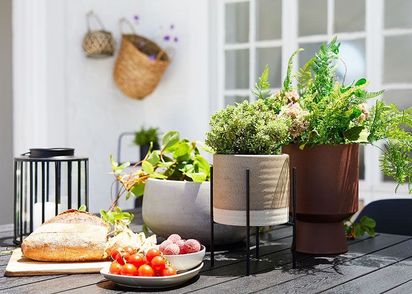 Ceramic plant pot, lantern and tray with bread and fruit on a garden table 