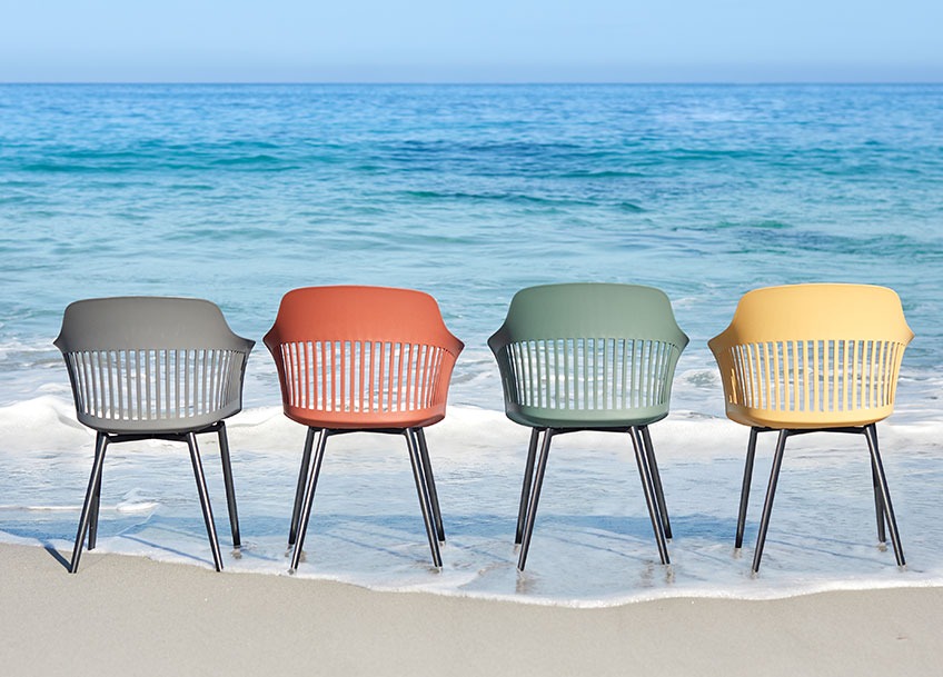 Four garden chairs in different colours on a beach 