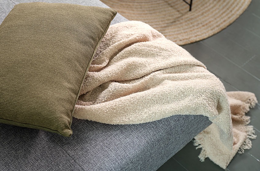 Green LILJE cushion and beige NATTLILJA throw A green cushion and a knitted throw on a grey sofa