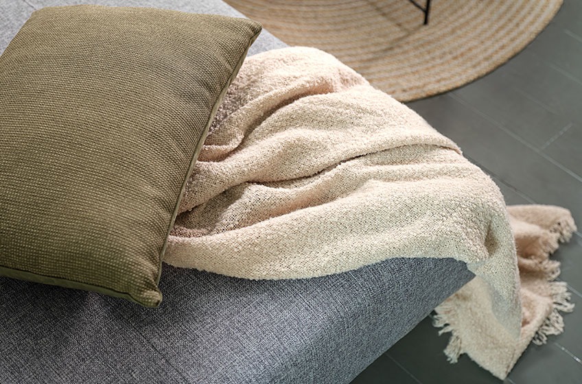 A green cushion and a knitted throw on a grey sofa