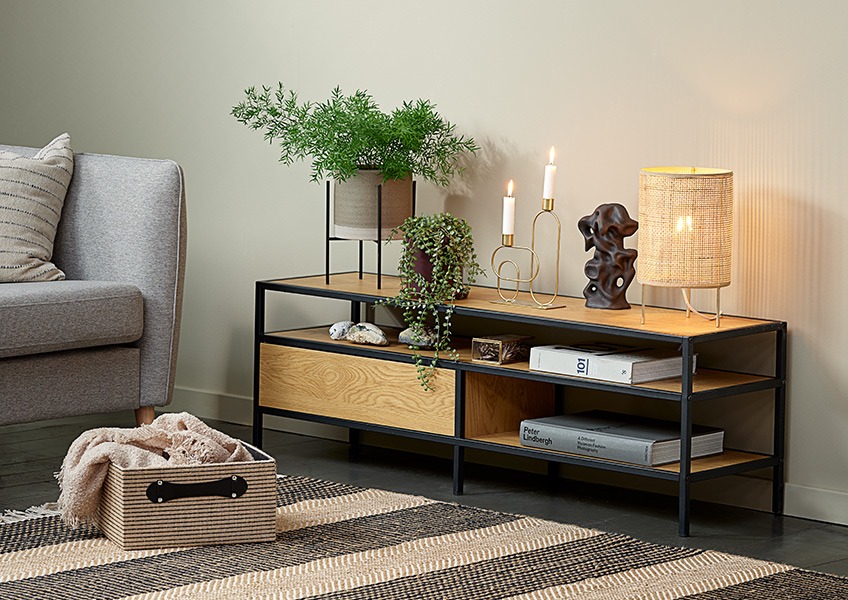 A corner of a living room with a sofa, a basket, a small table lamp and a modern TV stand