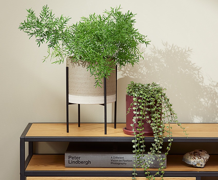 MANDRUP plant pot on legs and AXEL purple plant pot with SVENN artificial plant Two plant pots on a modern TV stand, one with a pointy plant and the other with a hanging plant